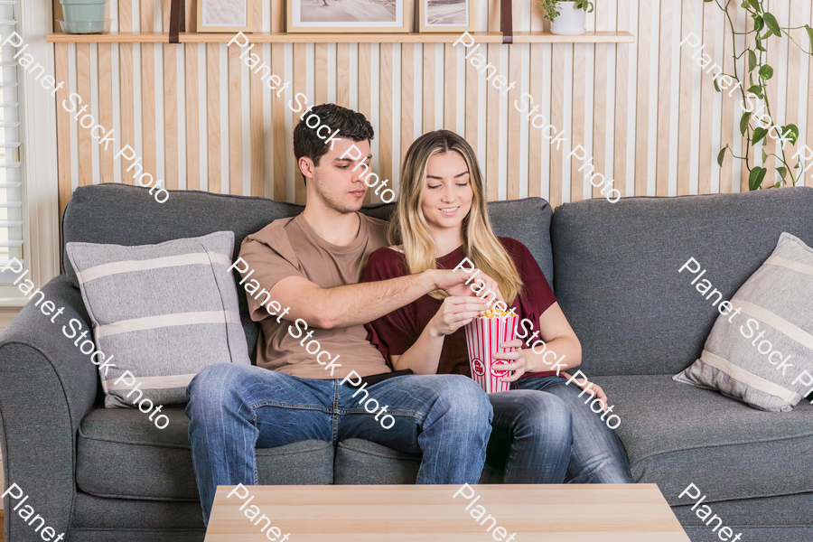 A young couple sitting on the couch, watching a movie, and enjoying popcorn stock photo with image ID: 0a31ea62-1dca-406e-affa-d8d6108da990