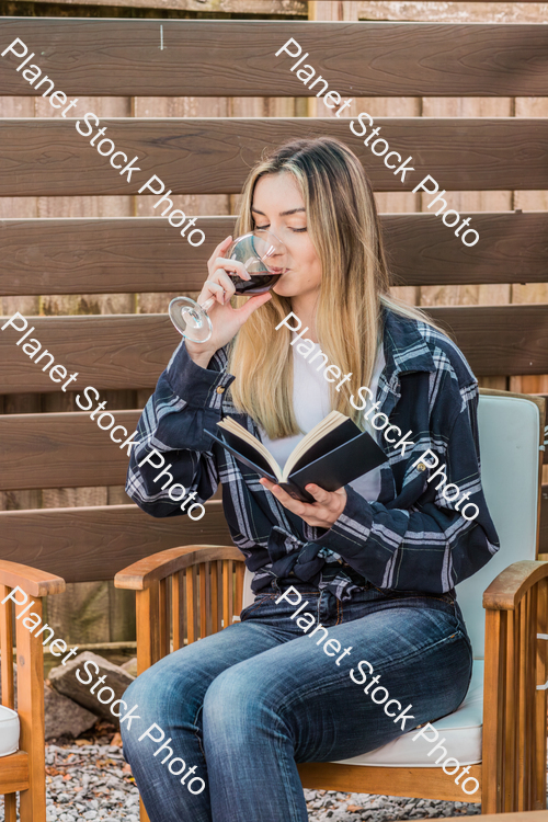 A young woman sitting outdoors reading a book and enjoying red wine stock photo with image ID: 12931a15-3bef-4a0c-ba9b-78545760b69c