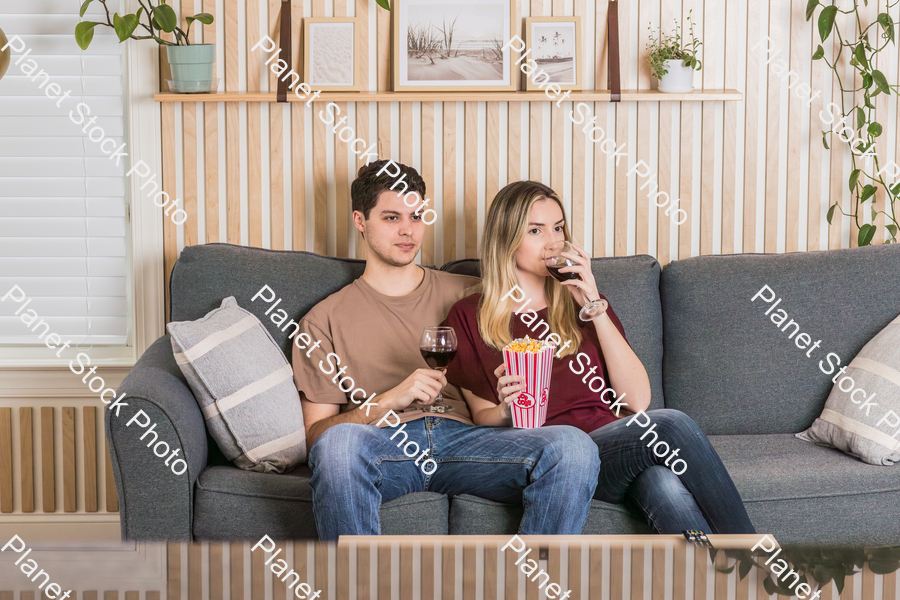 A young couple sitting on the sofa, watching a movie, and enjoying red wine and popcorn stock photo with image ID: 34303a82-a5b1-4b0b-9803-352efb0263f3