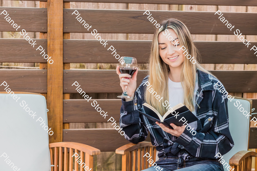 A young woman sitting outdoors reading a book, while enjoying red wine stock photo with image ID: 667cdbb1-70db-40bd-af61-ec5a610fc921