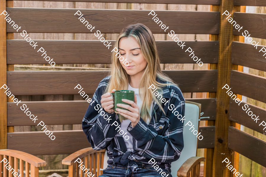 A young woman sitting outdoors enjoying a hot drink stock photo with image ID: 82727178-efe7-40cd-bb02-15890c92ba68