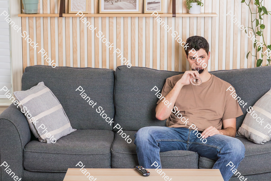 A young man sitting on the couch, watching a TV, and enjoying red wine stock photo with image ID: a8703721-bcd2-4965-bb05-7db5090d414d