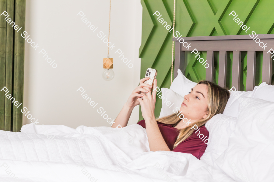 A young woman in bed using a mobile phone stock photo with image ID: b718303f-bbdc-4ab6-af1e-724f71146bb1
