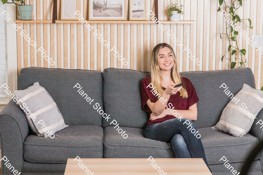 A young woman sitting on the couch watching TV stock photo with image ID: ba4e99ff-58bc-42ae-b074-de9c3ee0443b