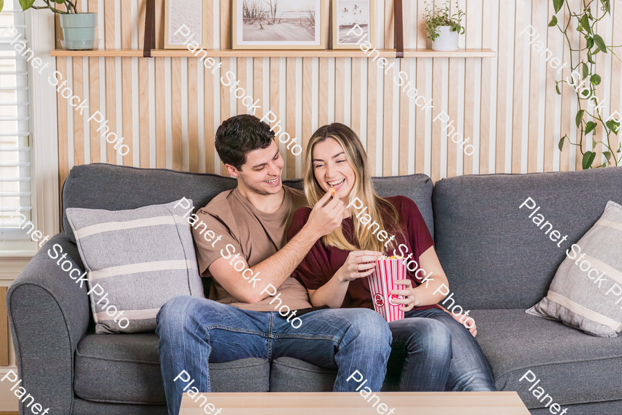 A young couple sitting on the couch, watching a movie, and enjoying popcorn stock photo with image ID: ebfcabd6-035c-4ffb-b2cc-f5702a436e0a
