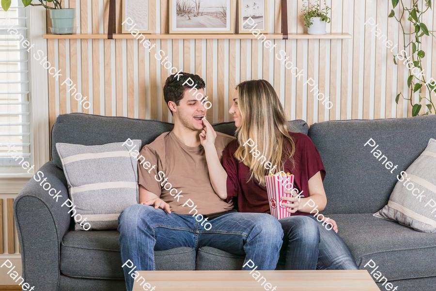 A young couple sitting on the couch, watching a movie, and enjoying popcorn stock photo with image ID: f4b017f8-006d-4139-b668-eafca1a88a6d