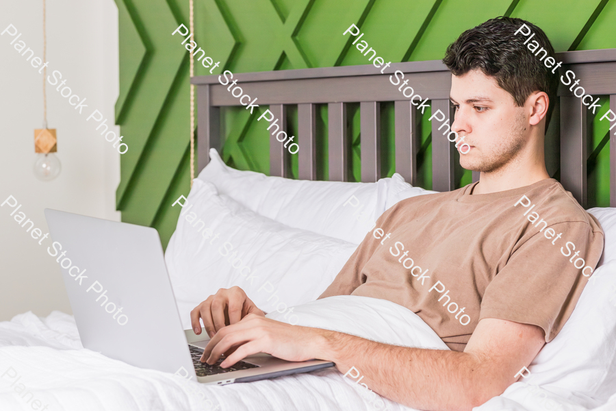 A young man in bed using a laptop stock photo with image ID: fdc4b045-d15e-4590-8d94-094a62c2dc15