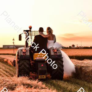 A Newly Married Couple Driving a Tractor Through the Grain Field Towards the Horizon at Sunset stock photo with image ID: 3555f6ec-458e-46e6-b6ca-2c93016440d6