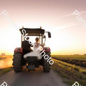 A Newly Married Couple Driving a Tractor Through the Grain Field Towards the Horizon at Sunset stock photo with image ID: 50da25a5-4e6d-4815-99e2-ebeb064de3bd
