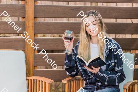 A young woman sitting outdoors reading a book, while enjoying red wine stock photo with image ID: 667cdbb1-70db-40bd-af61-ec5a610fc921