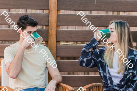 A young couple sitting outdoors, enjoying hot drinks stock photo with image ID: 6ec54902-5436-4081-bad7-4f132adcf3f5