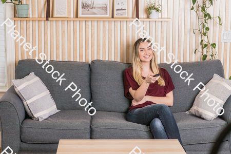 A young woman sitting on the couch watching TV stock photo with image ID: ba4e99ff-58bc-42ae-b074-de9c3ee0443b