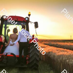 A Newly Married Couple Driving a Tractor Through the Grain Field Towards the Horizon at Sunset stock photo with image ID: fc06d38a-934c-4ed7-8a72-78038d0e01d8
