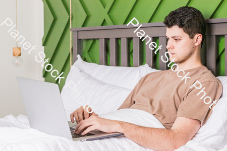 A young man in bed using a laptop stock photo with image ID: fdc4b045-d15e-4590-8d94-094a62c2dc15