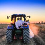 A Newly Married Couple Driving a Tractor Through the Grain Field Towards the Horizon at Sunset