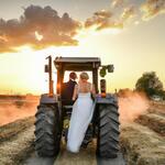 A Newly Married Couple Driving a Tractor Through the Grain Field Towards the Horizon at Sunset