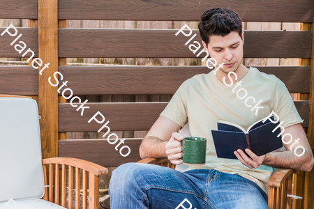 A young man sitting outdoors reading a book stock photo with image ID: a0efa301-8d39-46c9-b981-194c4d969758