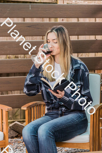 A young woman sitting outdoors reading a book and enjoying red wine stock photo with image ID: 12931a15-3bef-4a0c-ba9b-78545760b69c