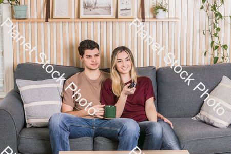 A young couple sitting on the couch watching a movie stock photo with image ID: d98c5195-3f6d-468d-be82-018ffd9f79fb