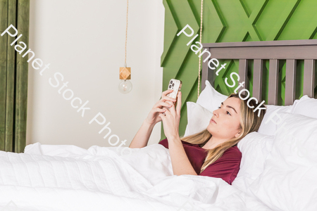 A young woman in bed using a mobile phone stock photo with image ID: b718303f-bbdc-4ab6-af1e-724f71146bb1