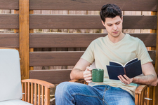A young man sitting outdoors reading a book