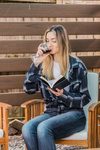 A young woman sitting outdoors reading a book and enjoying red wine
