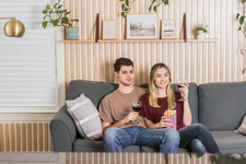 A young couple sitting on the sofa, watching a movie, and enjoying red wine and popcorn