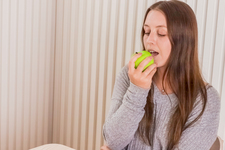 A girl sitting at the table, eating an apple