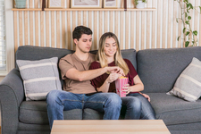 A young couple sitting on the couch, watching a movie, and enjoying popcorn