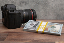 Three stacks of dollar-bills,  with a digital DSLR camera