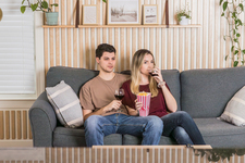 A young couple sitting on the sofa, watching a movie, and enjoying red wine and popcorn