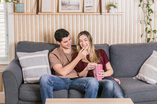 A young couple sitting on the couch, watching a movie, and enjoying popcorn